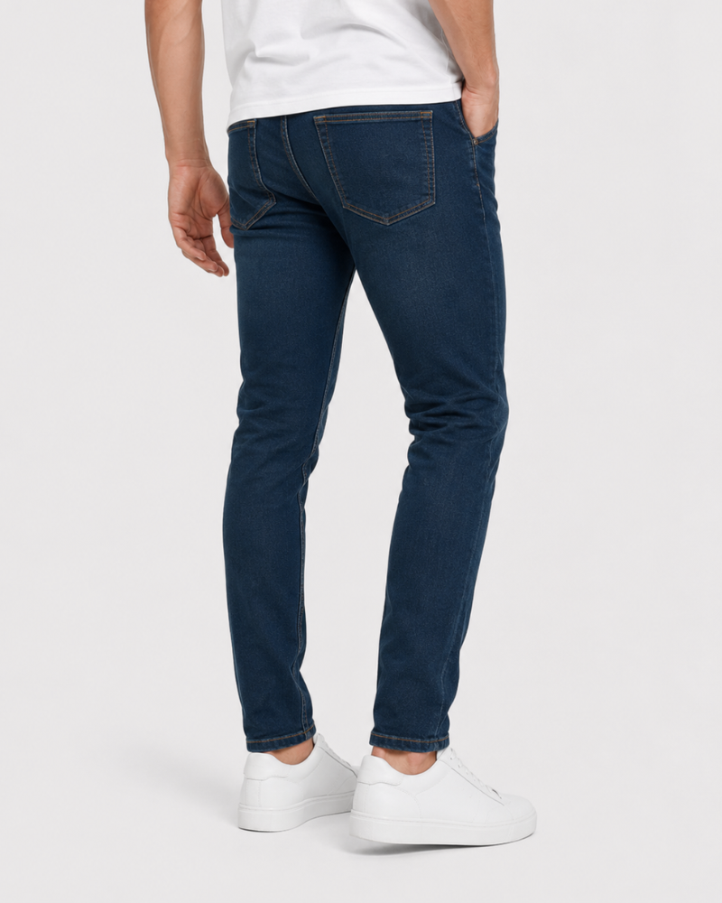 Grant Oak navy slim fit jeans worn by a male model, cropped back angle view, light grey background #Color_navy
