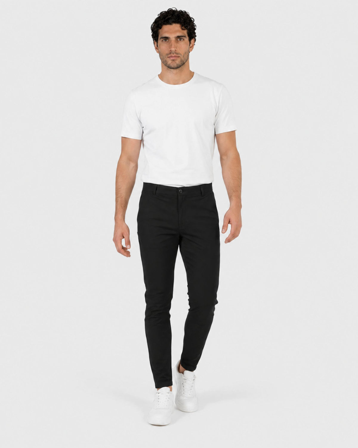 Grant Oak Smart Fit Chinos 2-Pack Black & Beige — man wearing a white crew-neck t-shirt and slim black chinos with white sneakers against a light gray studio background.