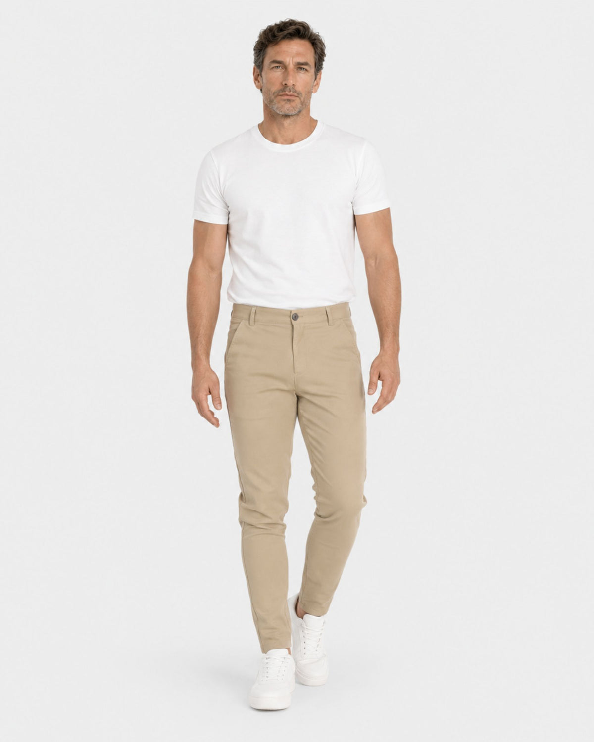 Grant Oak Smart Fit Chinos 4-Pack Essentials — man wearing slim-fit beige chinos with a white t-shirt and white sneakers against a light gray studio background.
