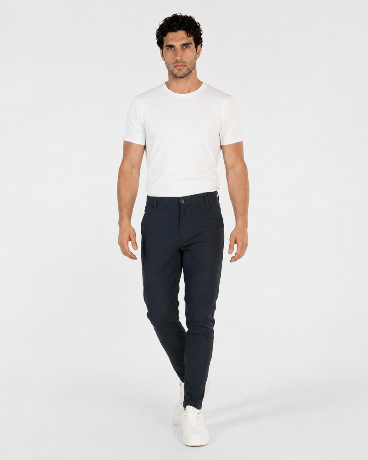 Grant Oak Smart Fit Chinos 4-Pack Essentials — man wearing a white short-sleeve crewneck t-shirt and dark navy blue slim-fit chinos with white sneakers against a light gray studio background.